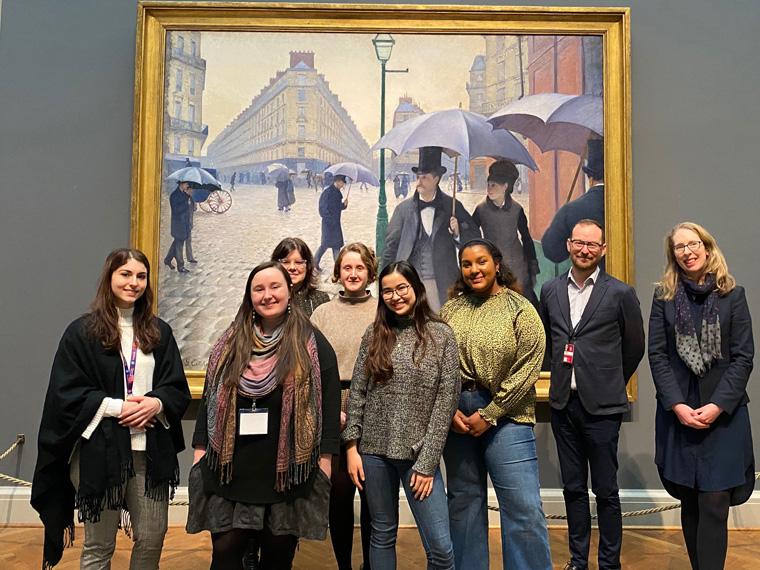 Group of students standing in front of 'Paris Street; Rainy Day' by Gustave Caillebotte.