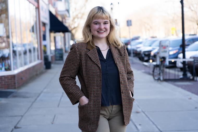 Blond woman standing in tweed jacket standing on street sidewalk.
