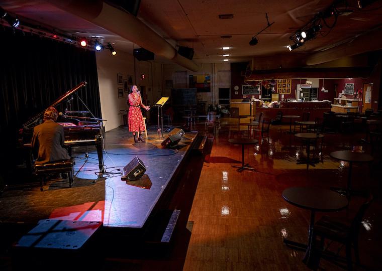 A student sings on a stage while a pianist plays nearby.