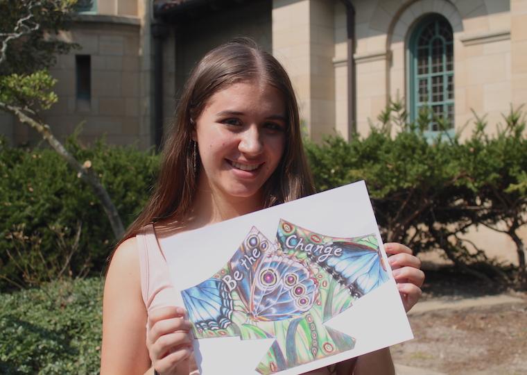 A girl holds a drawing of a mask.