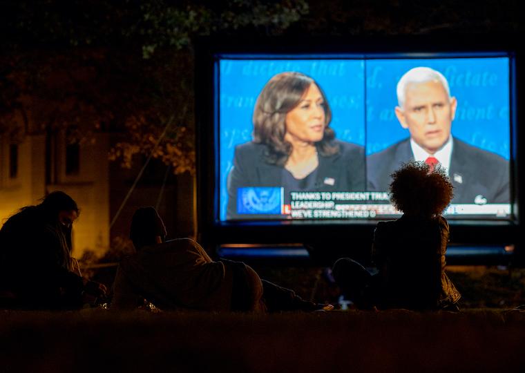 People look at a large screen with two people on it.