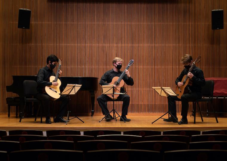 Three students play guitar on stage.