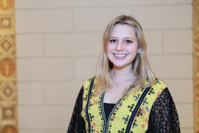 Jenna Gyimesi smiling while standing in front of a brick wall.