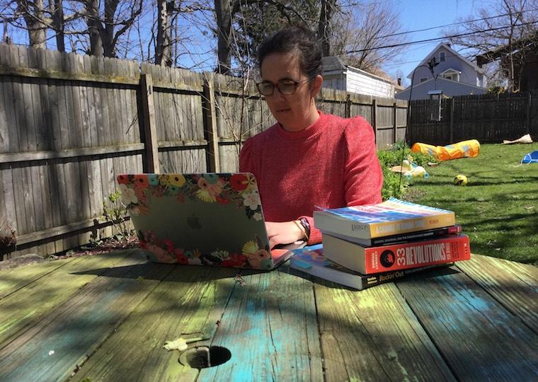 A woman types on a laptop in her backyard.