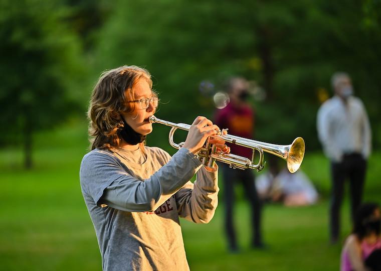 A student plays a trumpet in a park.