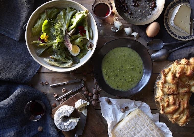 A table is filled with plates of cheese, salad, soup, and cake.