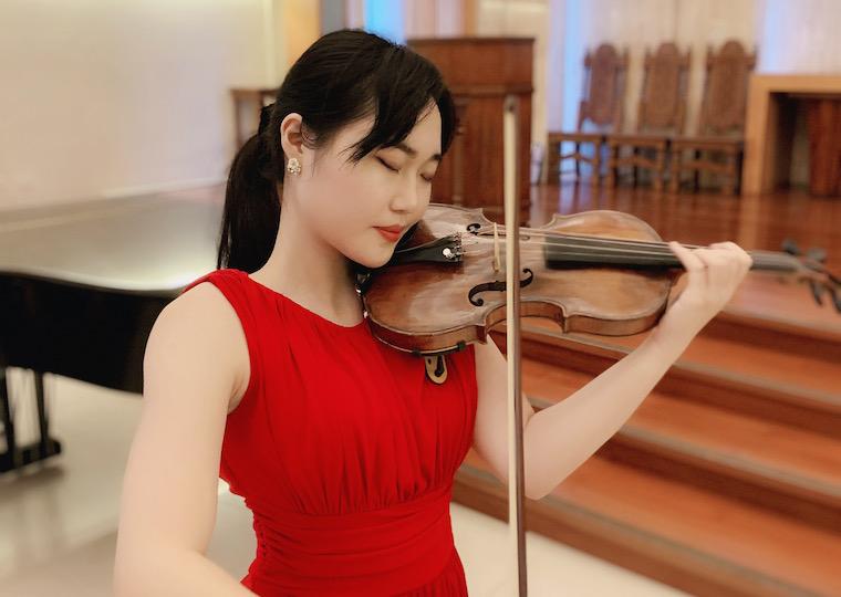 Asian girl in red dress plays a violin.
