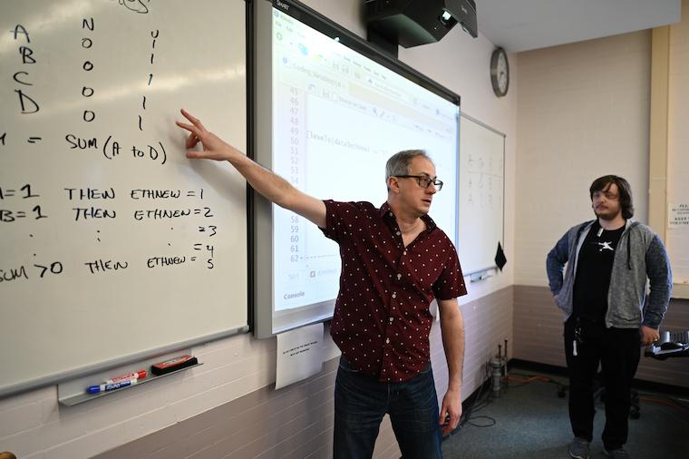 Man pointing at white board while a student looks on.