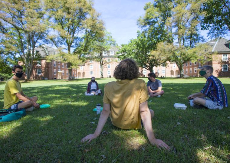 Students sit in a circle on a lawn.