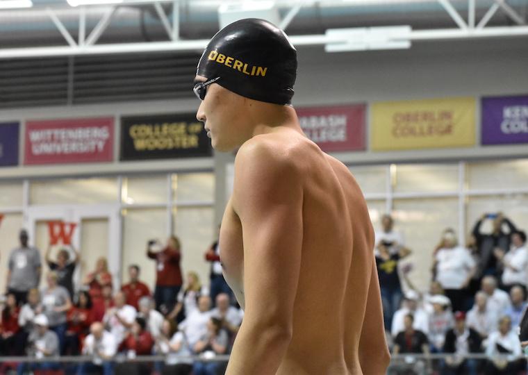A male swimmer stands with a crowd behind him.
