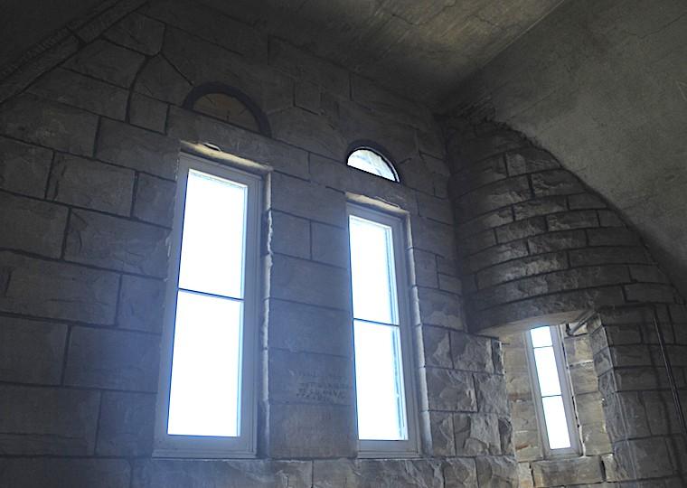 A stone wall with two windows and a long window on a circular wall.