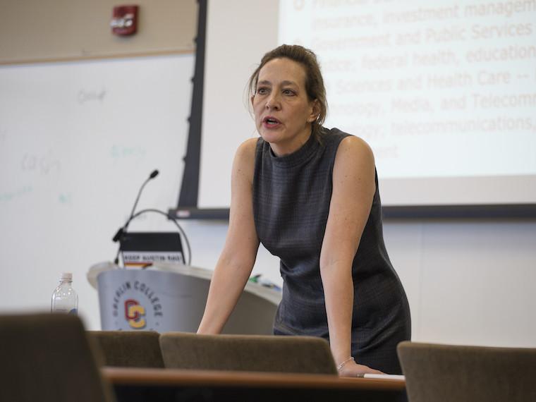woman leaning on a table near a podium with microphone.