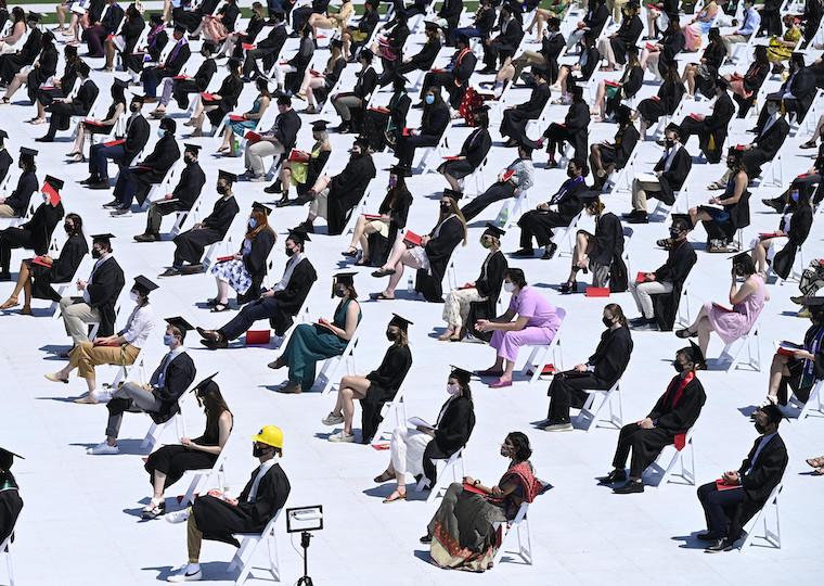 Alarge number od graduates sit 5 feet apart in a football field.