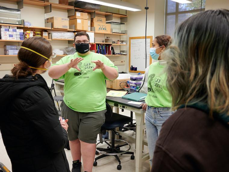 Students listen to a student talk in a lab.