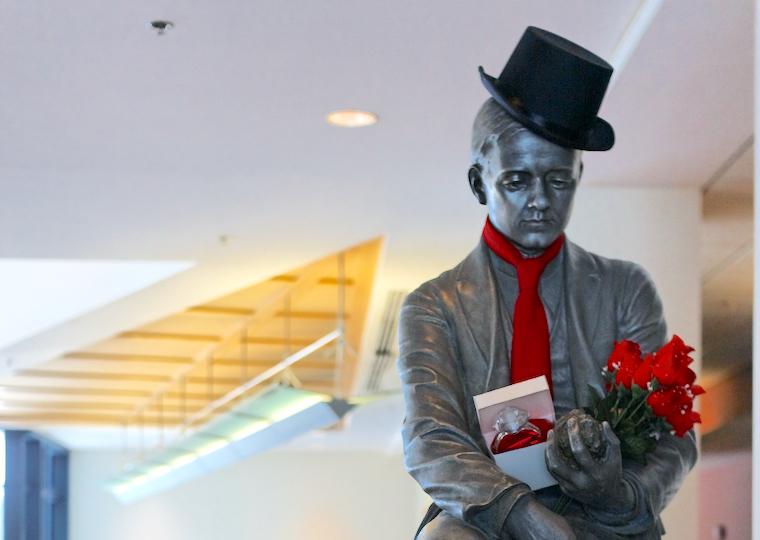 A statue of a man wearing a top hat and tie and carrying roses and a large diamond ring.