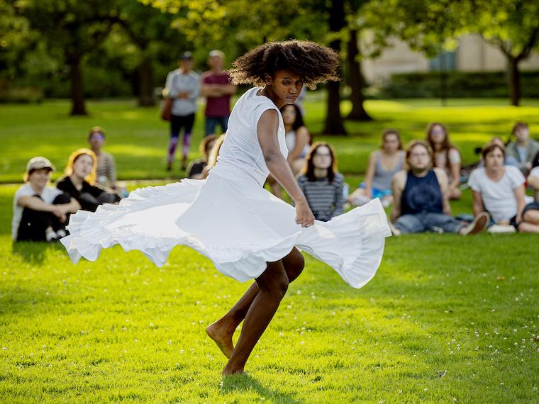A girl twirls around in a ruffled dress in front of an outdoor audience.