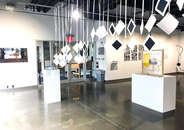 Small square cards hang from the ceiling in an art exhibit.