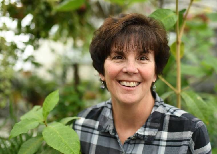 A portrait of a oman with plants behind her.