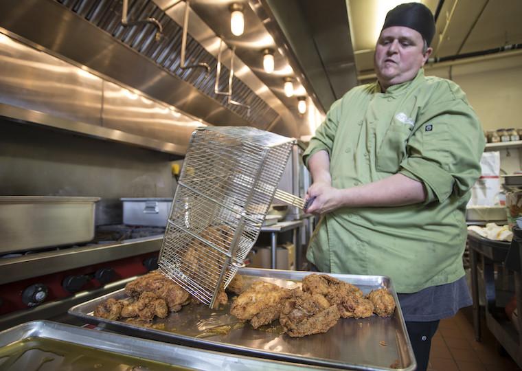 A man pours a basket of chicken onto a large tray.
