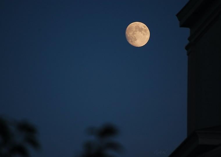 A full moon in a dark sky next to the silhouette of a building.