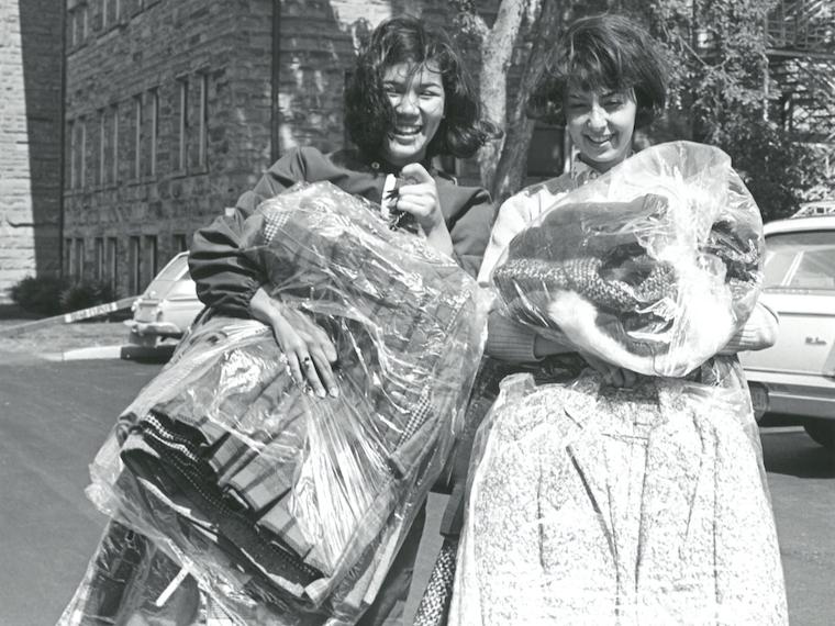 Two excited freshmen girls hold armloads of clothes.