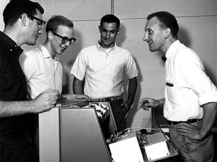 Students stand around Norm Craig as he demonstrates a spectrometer.