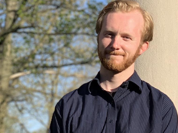 A portrait of a young man leaning on a stone column.