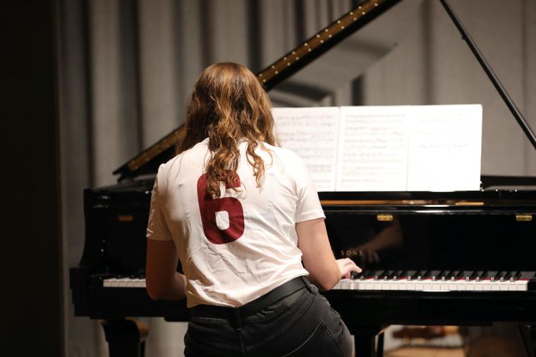 A student wearing a sports jersey plays the piano.