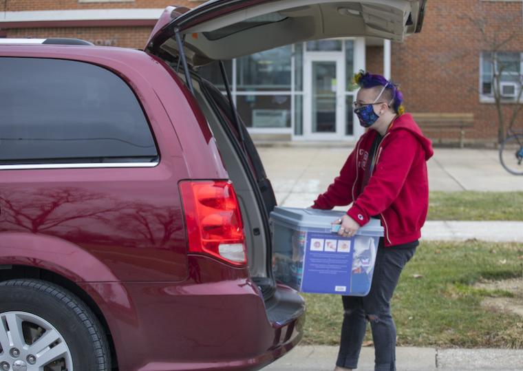 A student removes a large clear box from the trunk of a car.