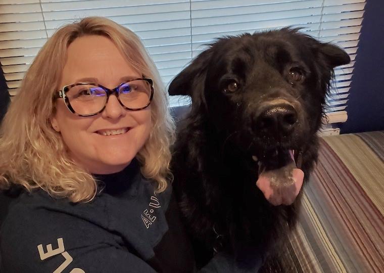 A woman smile at a camera while sitting next to her dog.