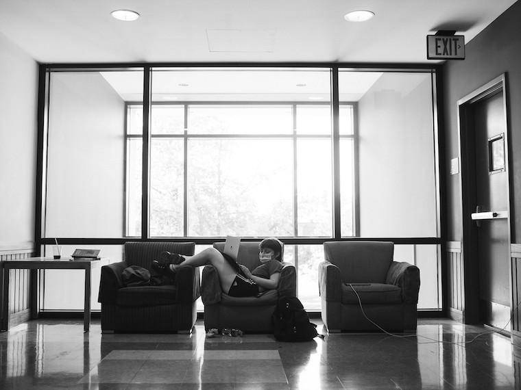A student lounging in a chair while working on a laptop.