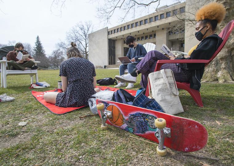 Students sit ion the lawn and in chairs as they study outside,