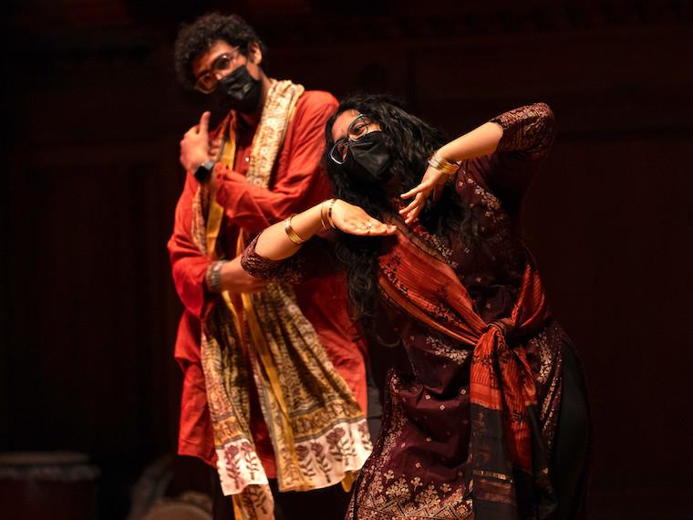 Two students wearing cultural robes dance on a stage.
