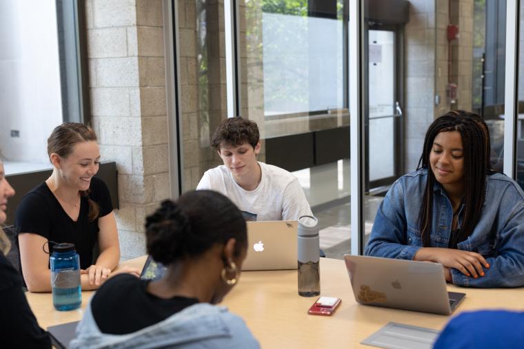 Students sitting around a conference table with computers.