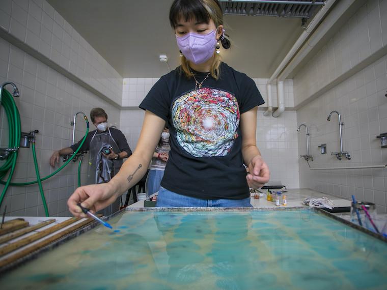 A student uses an eyedropper to add color to a tray of liquid.