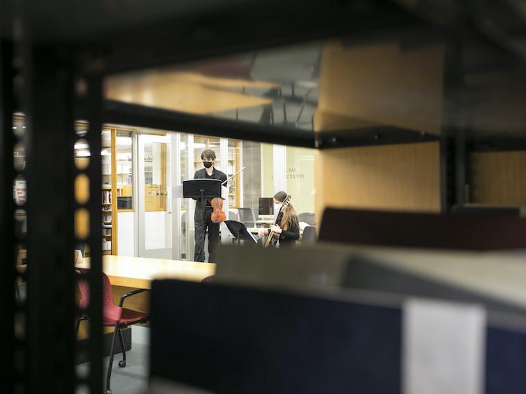 A violinist and guitarist play instruments in a library.