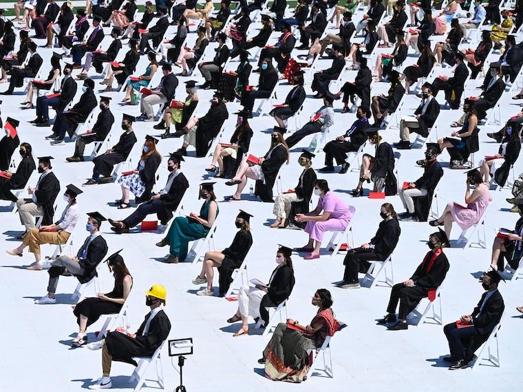 A large group of graduates sit socially distanced on a field.