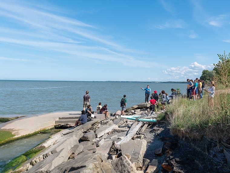 Students and professor stand on rocky lake shore