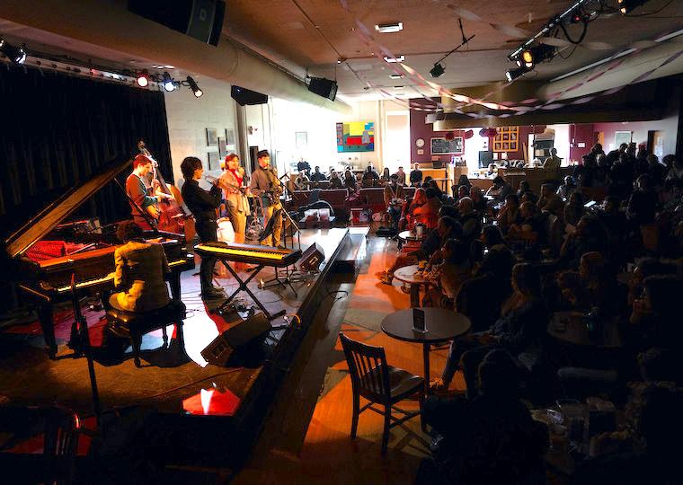 A large audience listens to a student jazz band on stage.