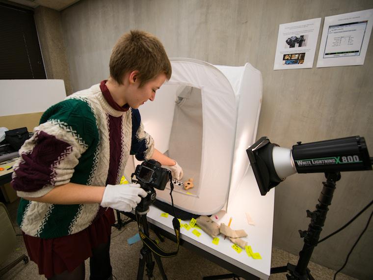 student with photo equipment taking picture of small artifact