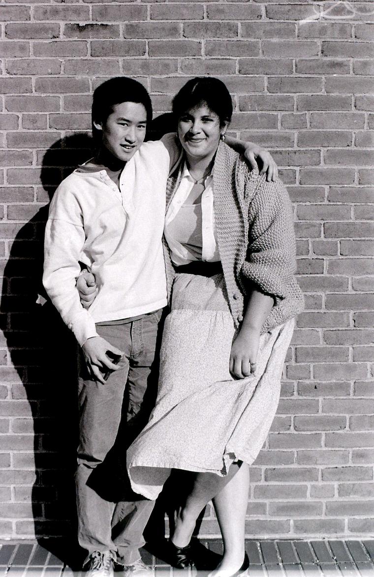 Two smiling students pose against a brick wall.