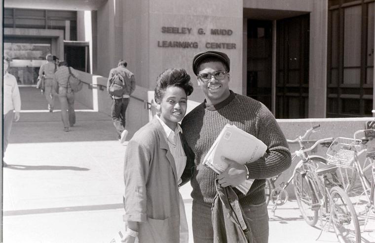 Two people pose outside the main entrance of Mudd Center.