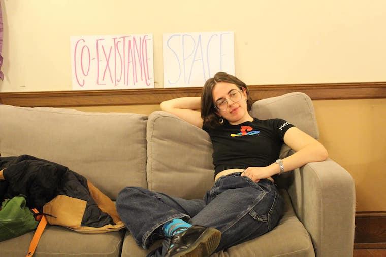 a woman leans on a couch with the sign "co-existance space" in the background