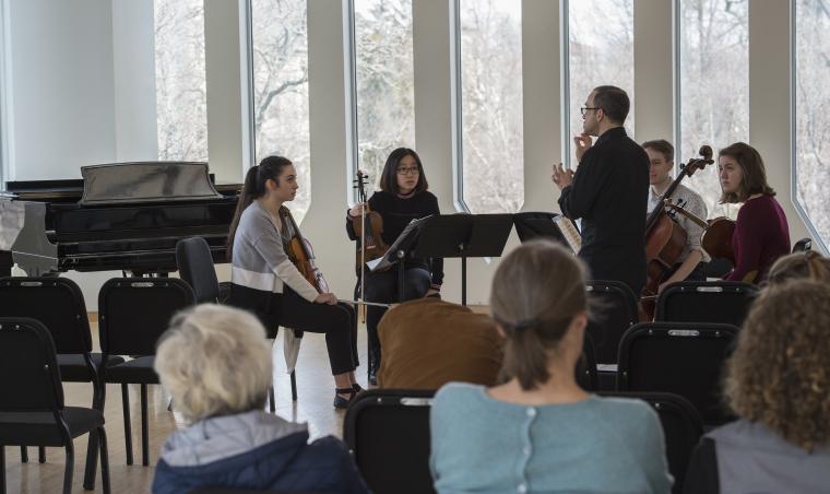 A man instructs a string quartet before an audience
