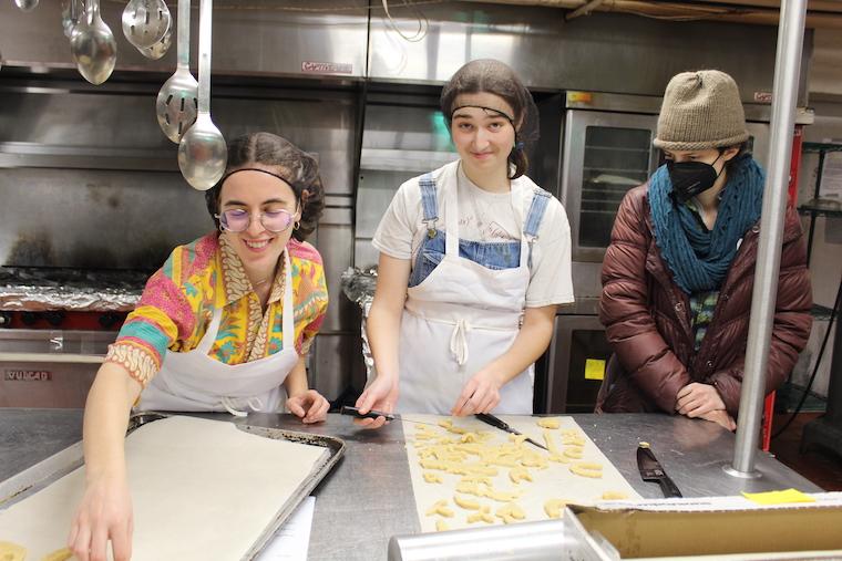 three people stand around a table where trays of sugar cookies are being made