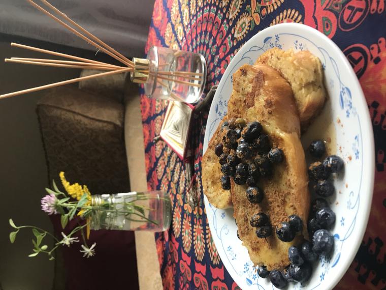 French toast with blueberries on a tablecloth with vase of flowers in the background