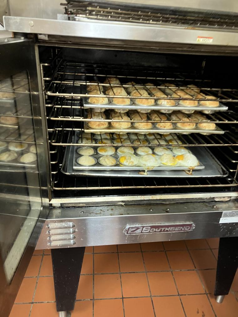 Picture of the inside of an oven. There are four racks. On the upper three racks there are rolls baking in muffin tins. On the lowest rack there are cooked sunny side up eggs baking in muffin tins.