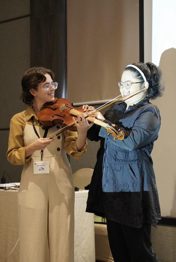 Ilana holds out her viola to a woman who holds on to it