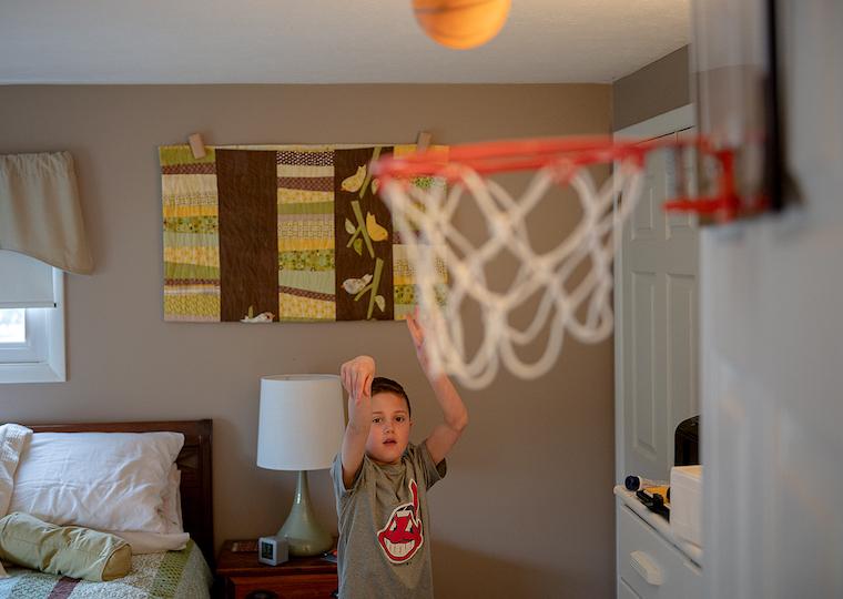 A boy playing basketball in his room.