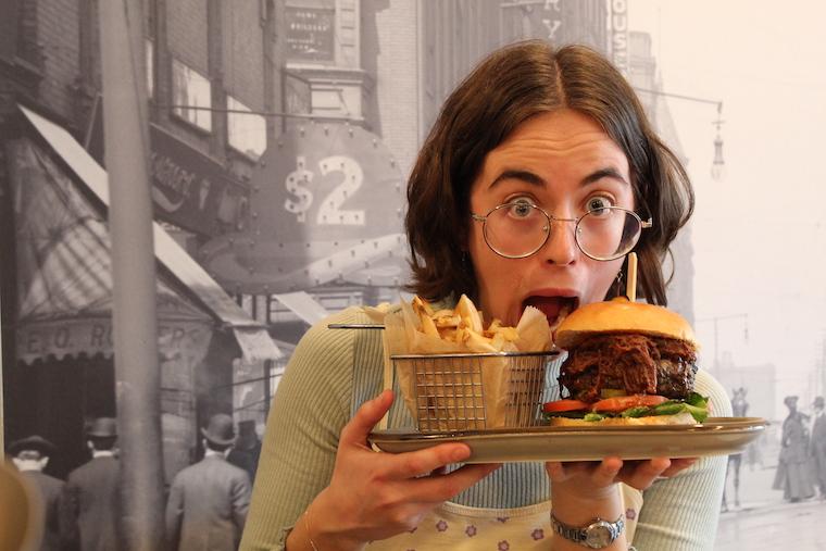 a woman holds up a huge burger and fries while making a funny face